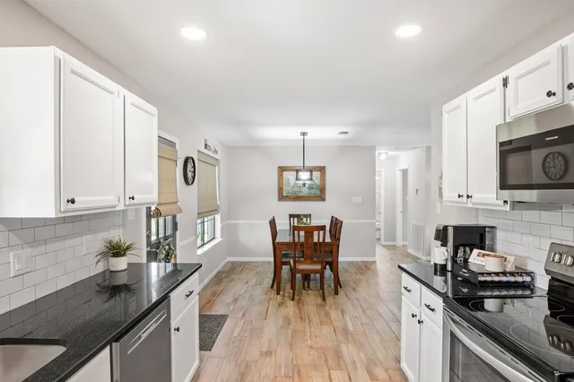 a kitchen with stainless steel appliances granite countertop a stove top oven a sink dishwasher a dining table and chairs with wooden floor