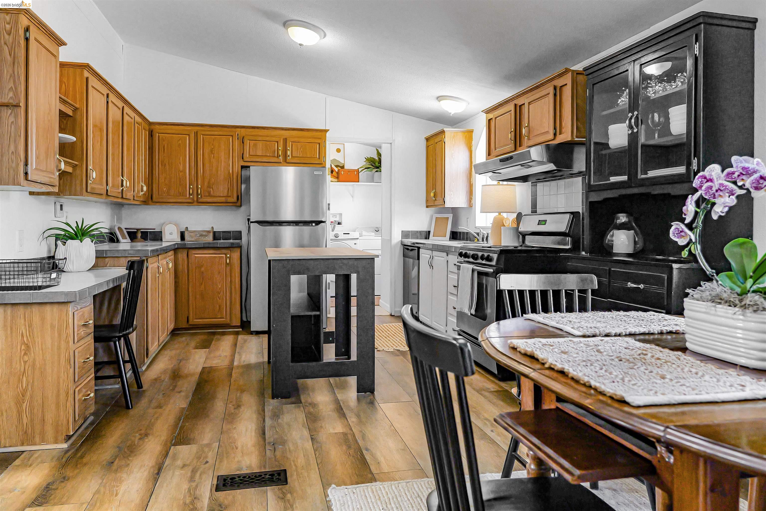 4419 Little John Road Copperopolis, CA 95228 - Photo 4 of 43 Open-concept kitchen featuring wood-finish flooring, a combination of wood cabinetry and black built-in storage with glass inserts, stainless steel appliances, and task lighting