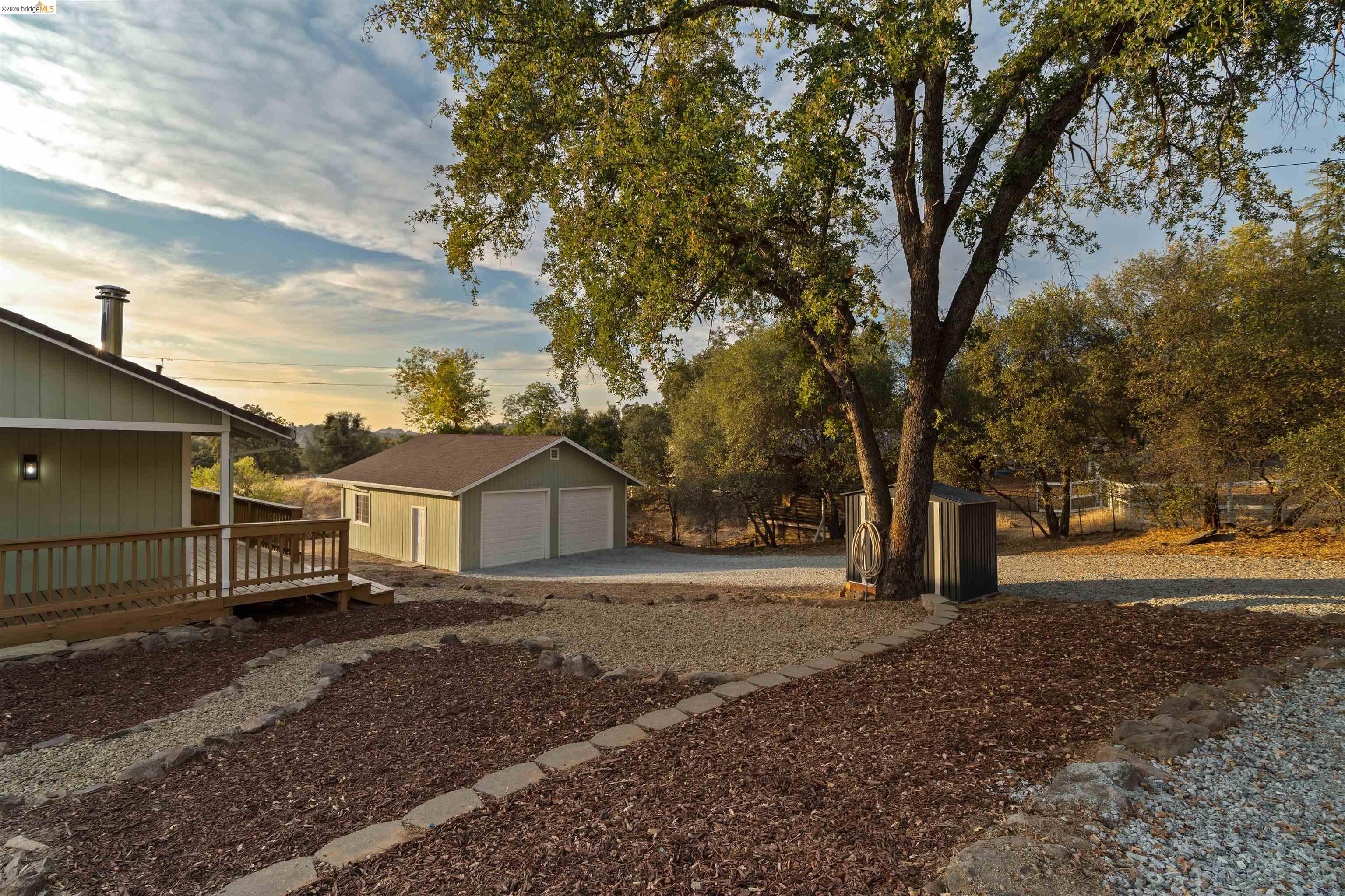 19676 Rawhide Road Sonora, CA 95370 - Photo 40 of 67 Exterior featuring a large wooden deck, detached garage with dual doors, gravel driveway, and mature landscaping