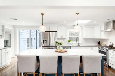 a kitchen with stainless steel appliances granite countertop a dining table chairs stove and white cabinets
