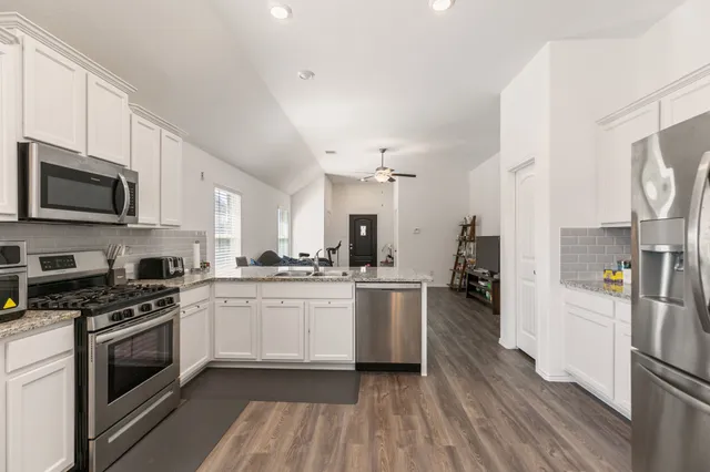 a kitchen with stainless steel appliances a stove top oven a sink dishwasher a refrigerator white cabinets and wooden floor