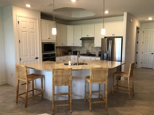 a kitchen with stainless steel appliances kitchen island granite countertop a table chairs refrigerator and microwave