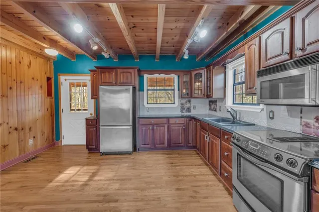 a kitchen with stainless steel appliances granite countertop a refrigerator a sink dishwasher a stove a dining table and chairs with wooden floor