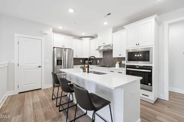 a kitchen with stainless steel appliances a dining table chairs refrigerator and sink