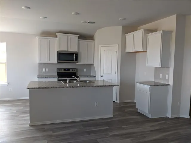 a kitchen with stainless steel appliances granite countertop a stove top oven a sink a refrigerator white cabinets and wooden floor