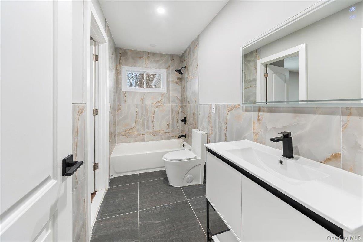 96 Fairmont Road Mahopac, NY 10541 - Photo 16 of 34 Bathroom with a contemporary vanity, black fixtures, tiled floor, a bathtub with a tiled surround, and a compact window