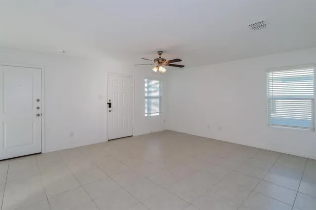an empty room with chandelier fan and windows