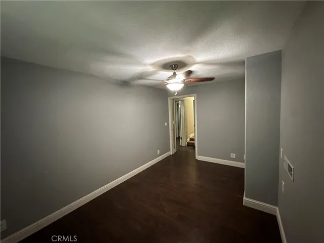 a view of an empty room with wooden floor and a ceiling fan