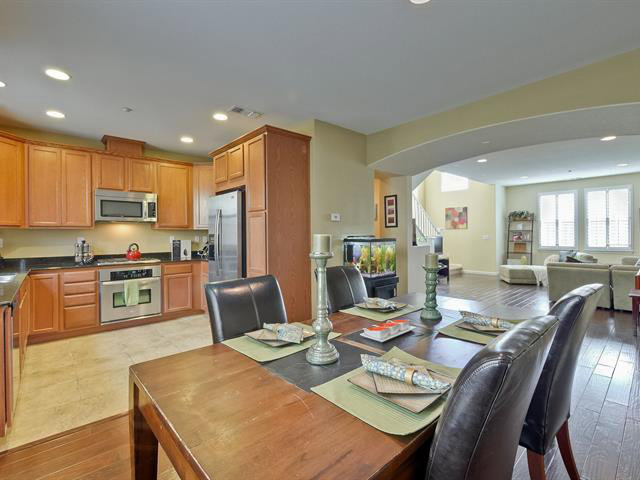 a open dining room with stainless steel appliances granite countertop a stove a refrigerator a couch a dining table and chairs with wooden floor