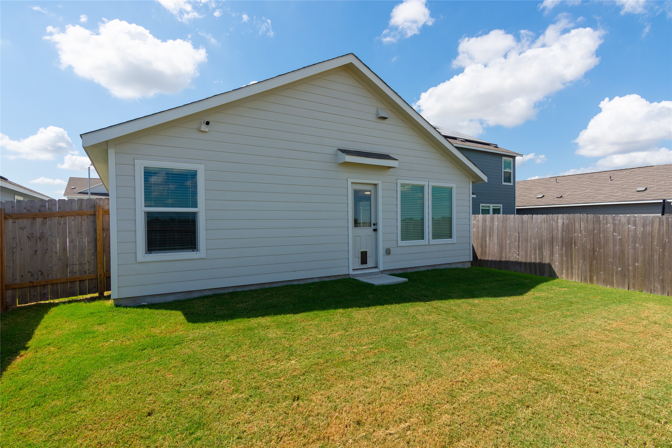 548 Rancho Del Cielo Loop Jarrell, TX 76537 - Photo 28 of 40 Exterior featuring siding, multiple windows, a rear entry door, and a private fenced yard with a grass lawn