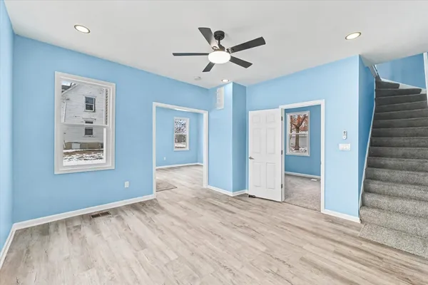a view of an empty room with wooden floor and a ceiling fan