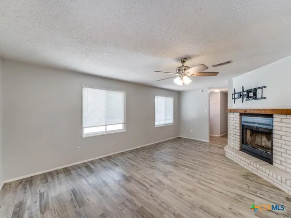 a view of an empty room with wooden floor fireplace and a window
