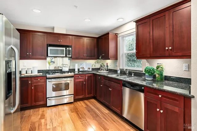 a kitchen with stainless steel appliances granite countertop wooden cabinets a stove top oven a sink and dishwasher with wooden floor