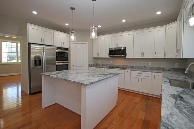 a kitchen with kitchen island granite countertop a stove a sink a refrigerator and white cabinets with wooden floor