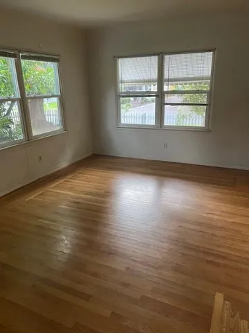 a view of an empty room with wooden floor and windows