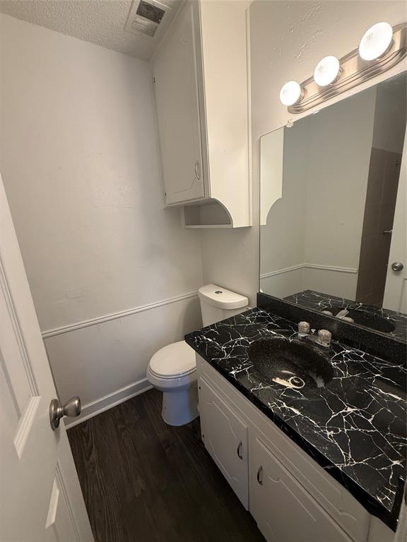 708 East Pecan Street, Unit 712 Hurst, TX 76053 - Photo 13 of 15 Bathroom featuring a black vanity with a white-veined countertop, white cabinetry, a built-in mirror, and wood-finish flooring