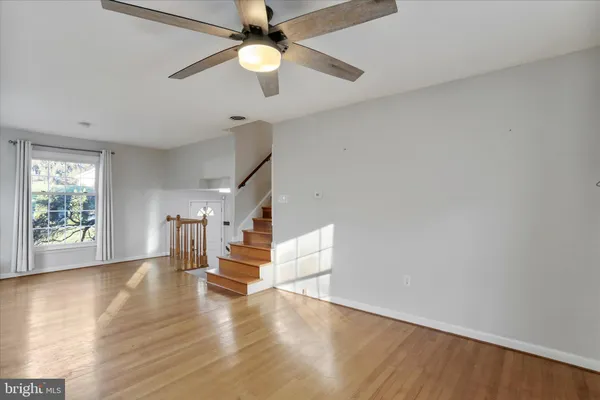 an empty room with wooden floor chandelier fan and windows