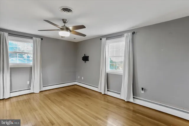 an empty room with wooden floor chandelier fan and windows