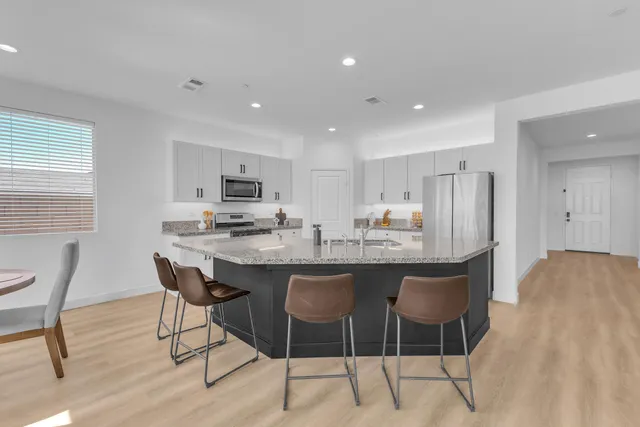 a kitchen with stainless steel appliances kitchen island granite countertop a dining table chairs and a refrigerator