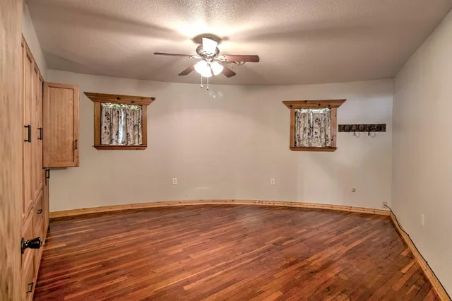 an empty room with wooden floor chandelier fan and windows