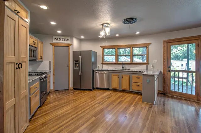 a kitchen with stainless steel appliances kitchen island granite countertop a refrigerator a sink dishwasher a stove and a dining table with wooden floor