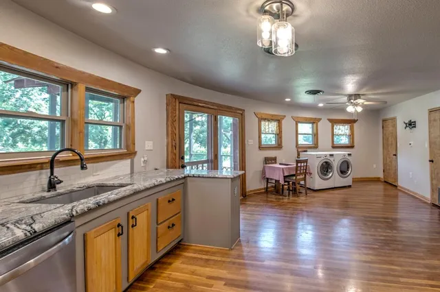 a very nice looking kitchen with granite countertop a large window cabinets and wooden floor