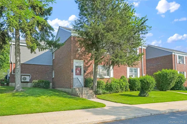a view of a brick house next to a yard with potted plants and large trees