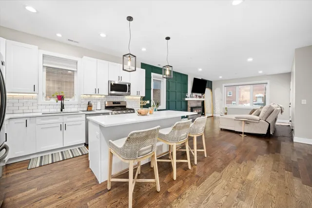 a kitchen with stainless steel appliances kitchen island granite countertop a stove a sink a refrigerator and white cabinets with wooden floor