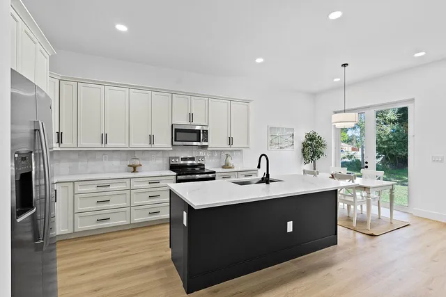 a kitchen with stainless steel appliances kitchen island granite countertop a sink dishwasher a stove a refrigerator and white cabinets with wooden floor