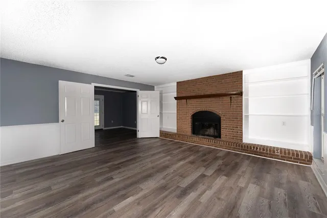 a view of an empty room with wooden floor fireplace and a window
