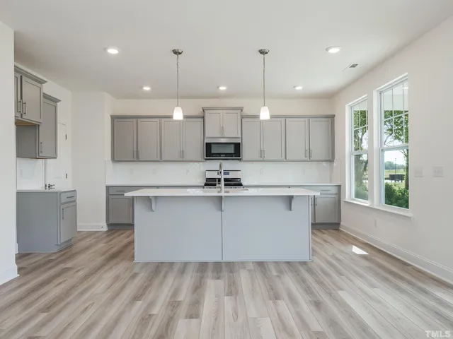 a large white kitchen with kitchen island wooden floors white cabinets and stainless steel appliances