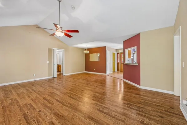 a view of an empty room with wooden floor and a ceiling fan