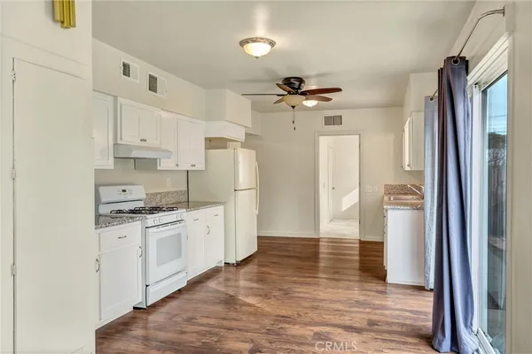 a kitchen with stainless steel appliances granite countertop a refrigerator a stove a sink and white cabinets with wooden floor