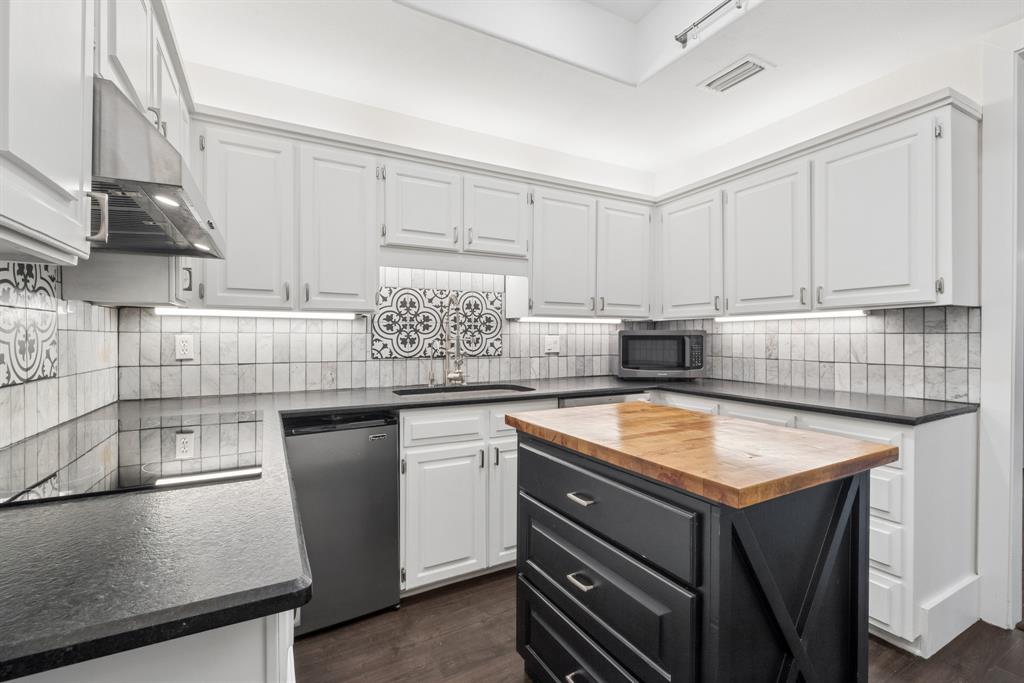 15539 Preston Road, Unit 1037 Dallas, TX 75248 - Photo 9 of 36 White shaker-style cabinetry with dark countertops, a custom butcher block island, stainless steel dishwasher, and a decorative tile backsplash