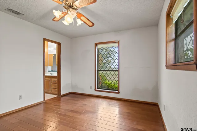 an empty room with wooden floor chandelier fan and windows