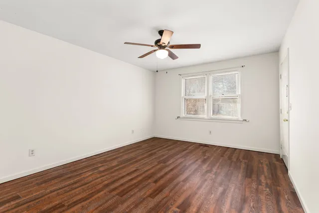 an empty room with wooden floor ceiling fan and windows