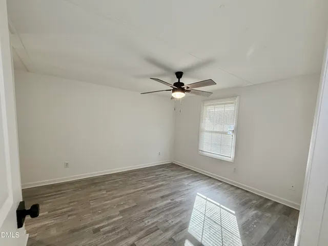 an empty room with wooden floor fan and windows