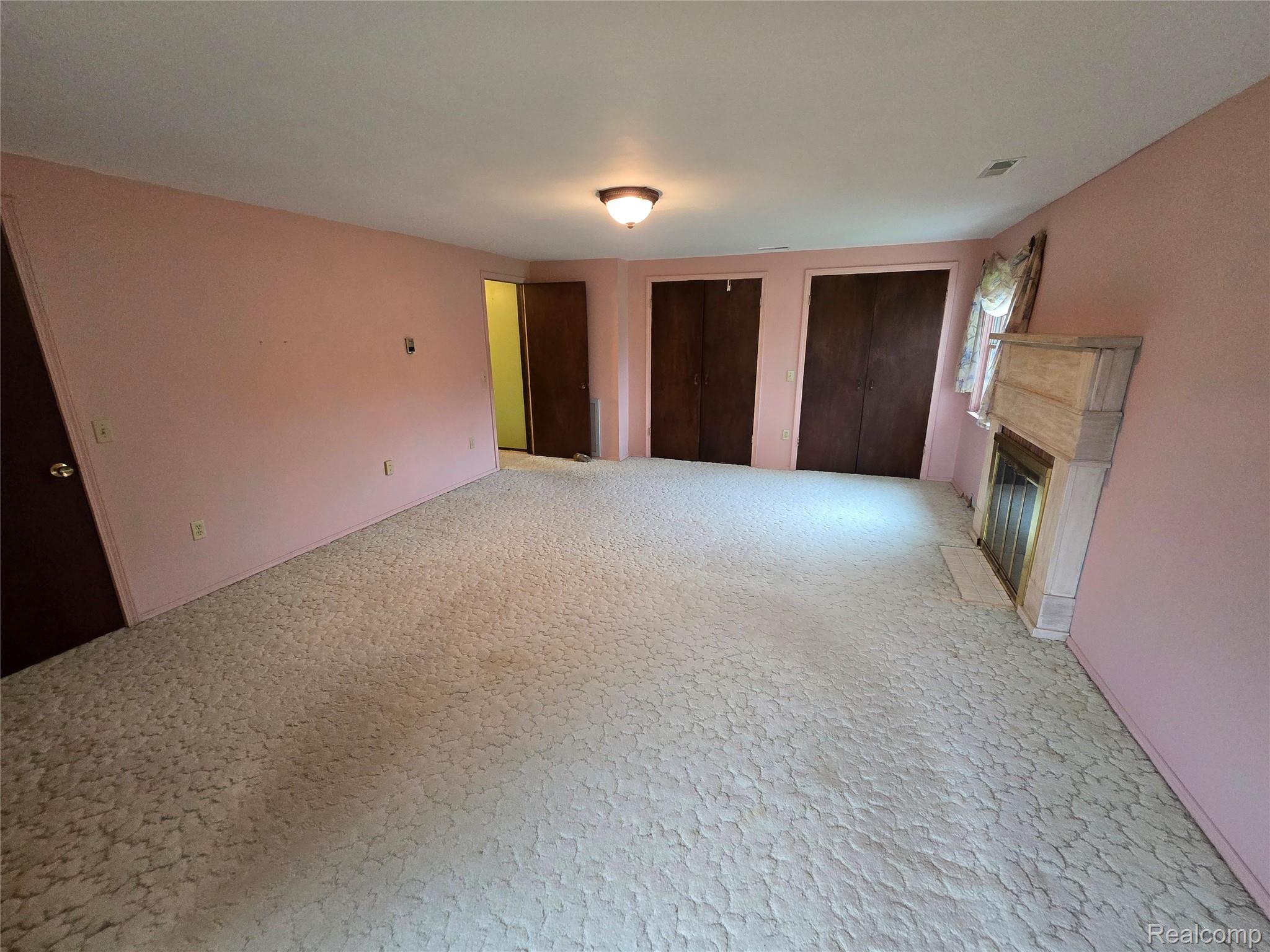 5282 McIntyre Road North Street, MI 48049 - Photo 38 of 53 Carpeted room featuring a fireplace with a light-toned surround, two integrated closets with dark wood-finish doors, a flush-mount ceiling light fixture, and an additional dark wood-finish door