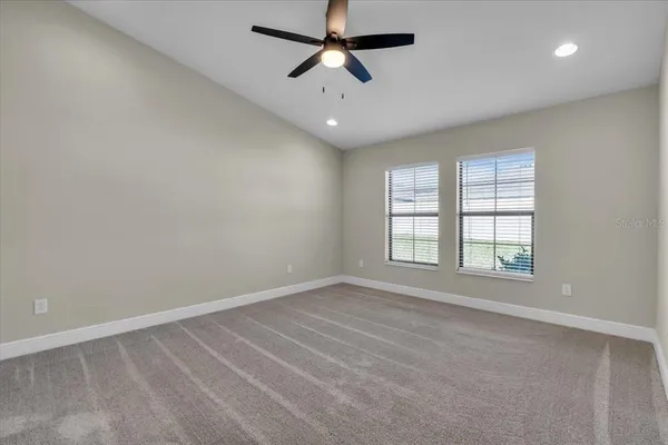 an empty room with chandelier fan and windows