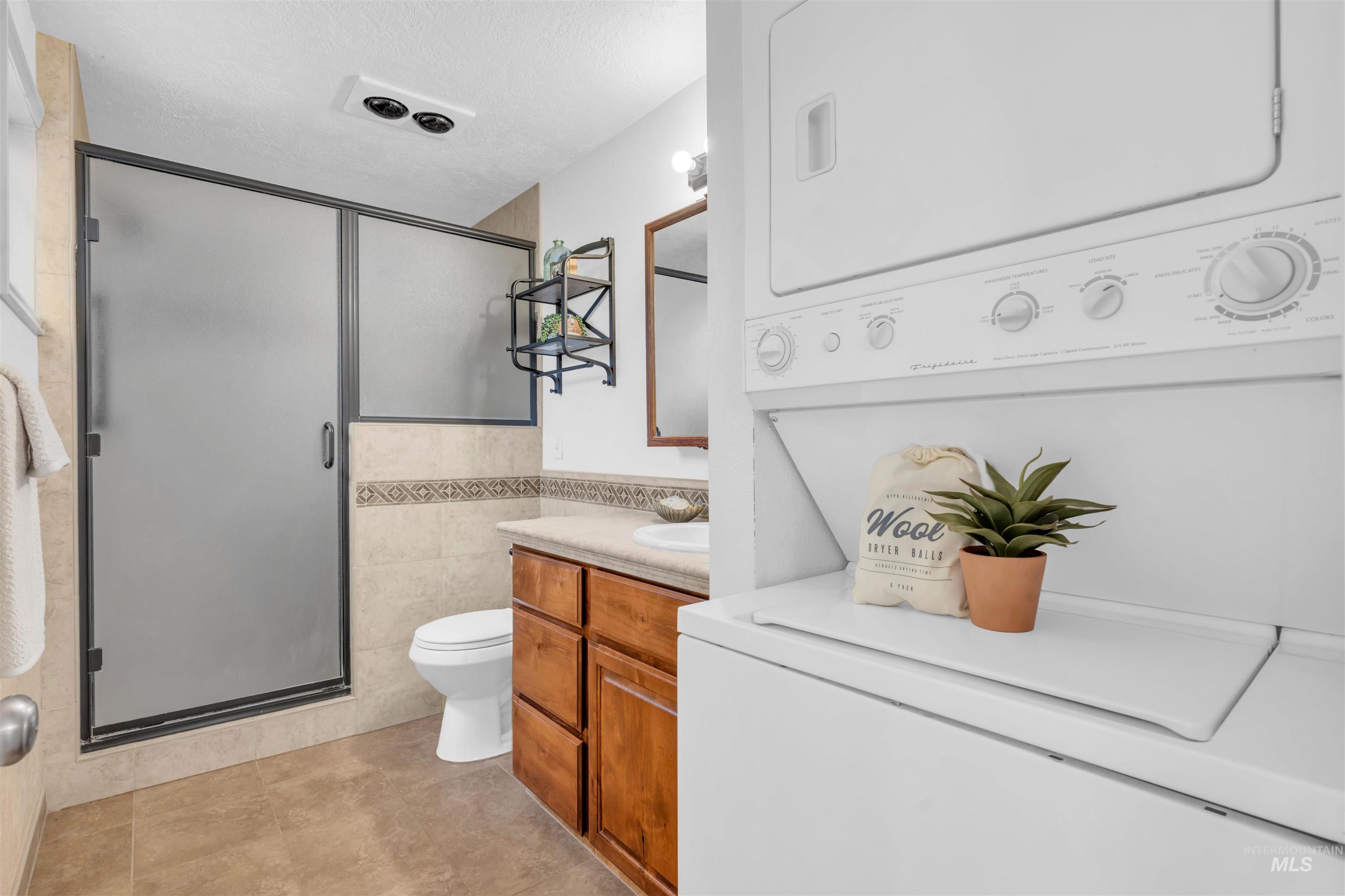 120 South Locust Street Nampa, ID 83686 - Photo 11 of 32 Full bathroom featuring tile walls, vanity, a stall shower, a textured ceiling, and stacked washing machine and dryer