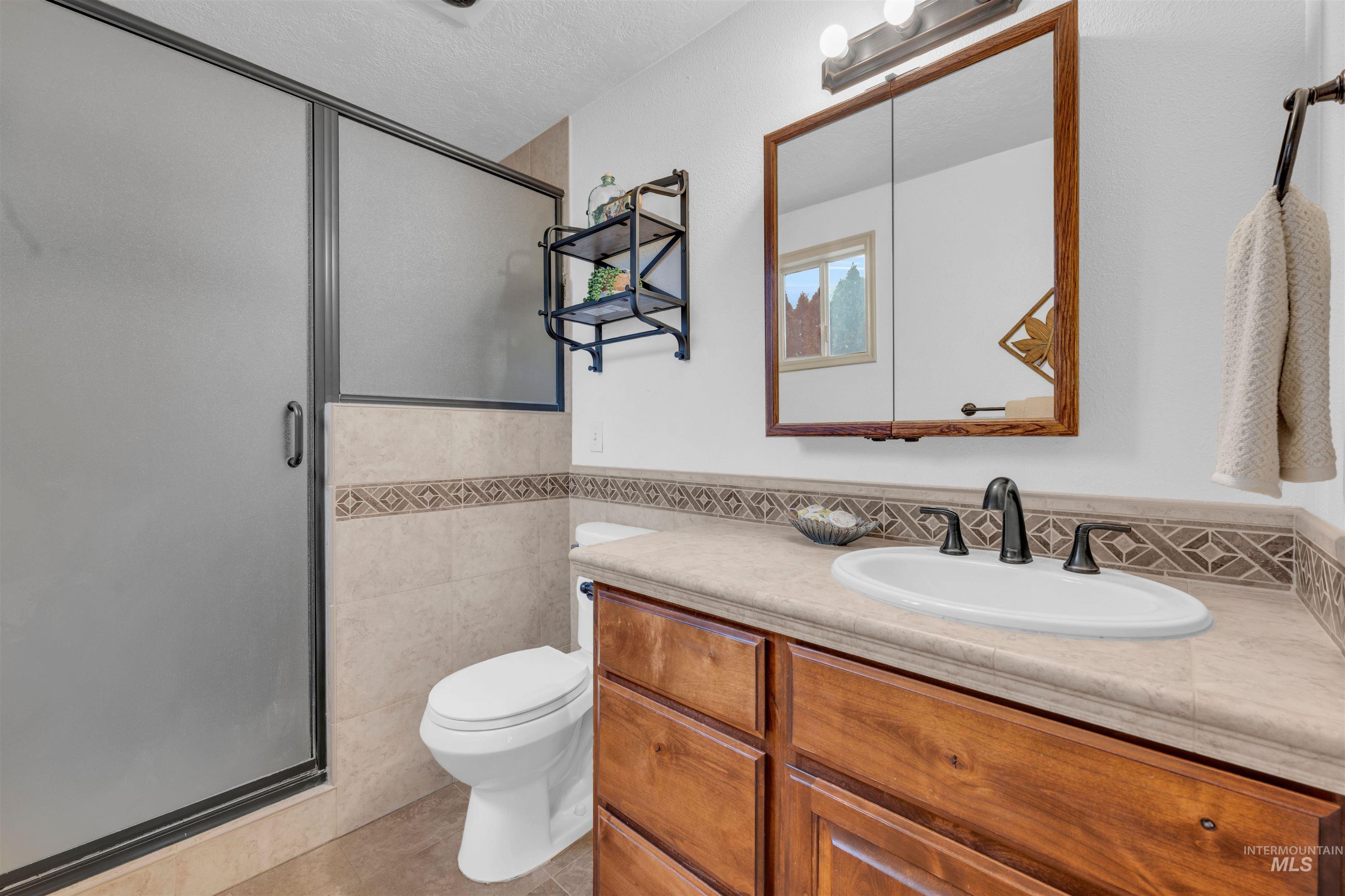 120 South Locust Street Nampa, ID 83686 - Photo 12 of 32 Full bathroom with tile walls, vanity, a stall shower, a textured ceiling, and light tile patterned flooring