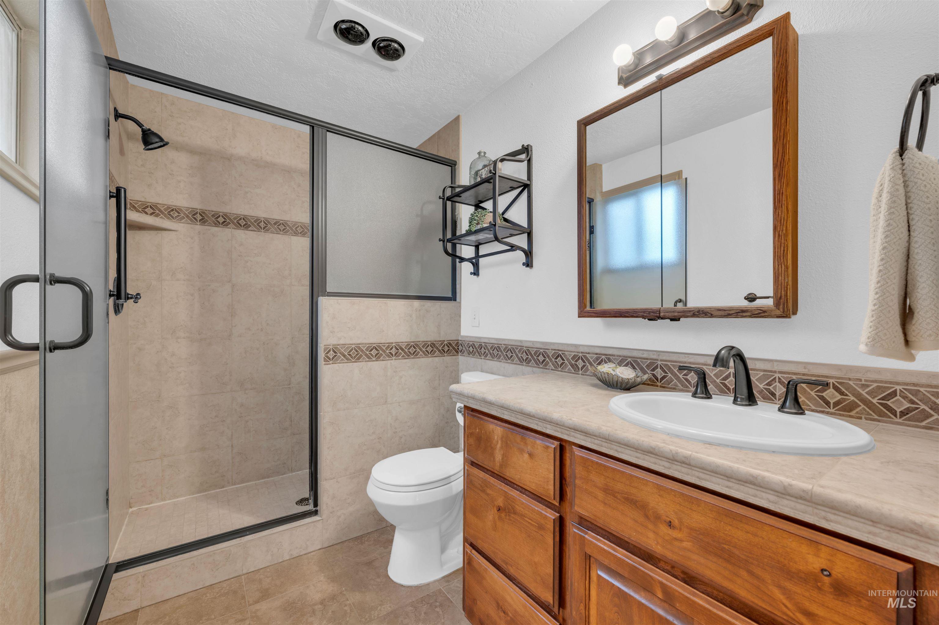 120 South Locust Street Nampa, ID 83686 - Photo 14 of 32 Full bath with vanity, a stall shower, a textured ceiling, tile walls, and a wainscoted wall