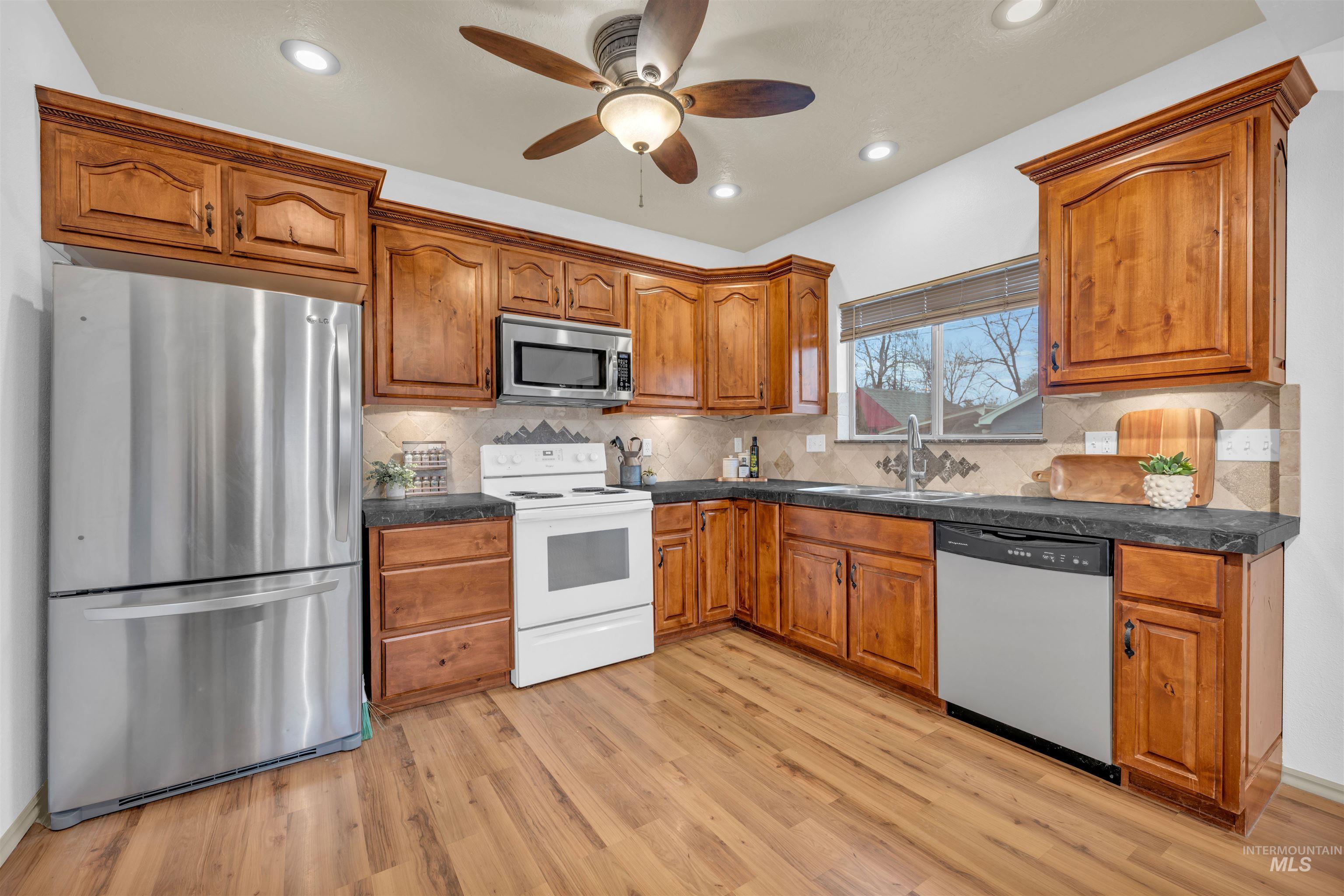 120 South Locust Street Nampa, ID 83686 - Photo 16 of 32 Kitchen featuring appliances with stainless steel finishes, brown cabinets, dark countertops, ceiling fan, and light wood-style floors