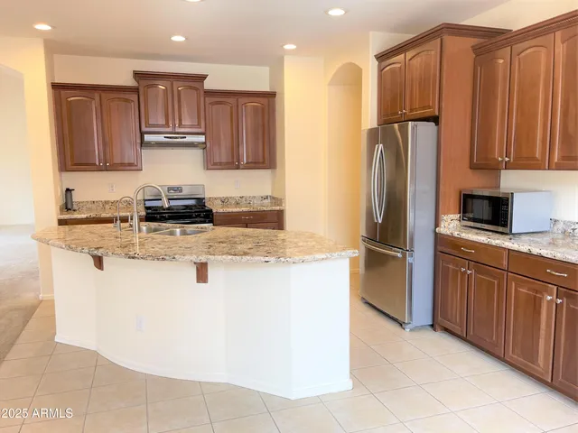 a kitchen with kitchen island granite countertop wooden cabinets a refrigerator and a sink