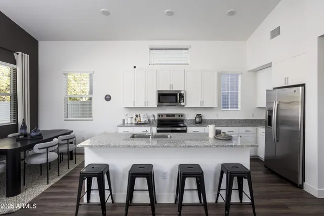 a kitchen with stainless steel appliances granite countertop a dining table chairs refrigerator and sink