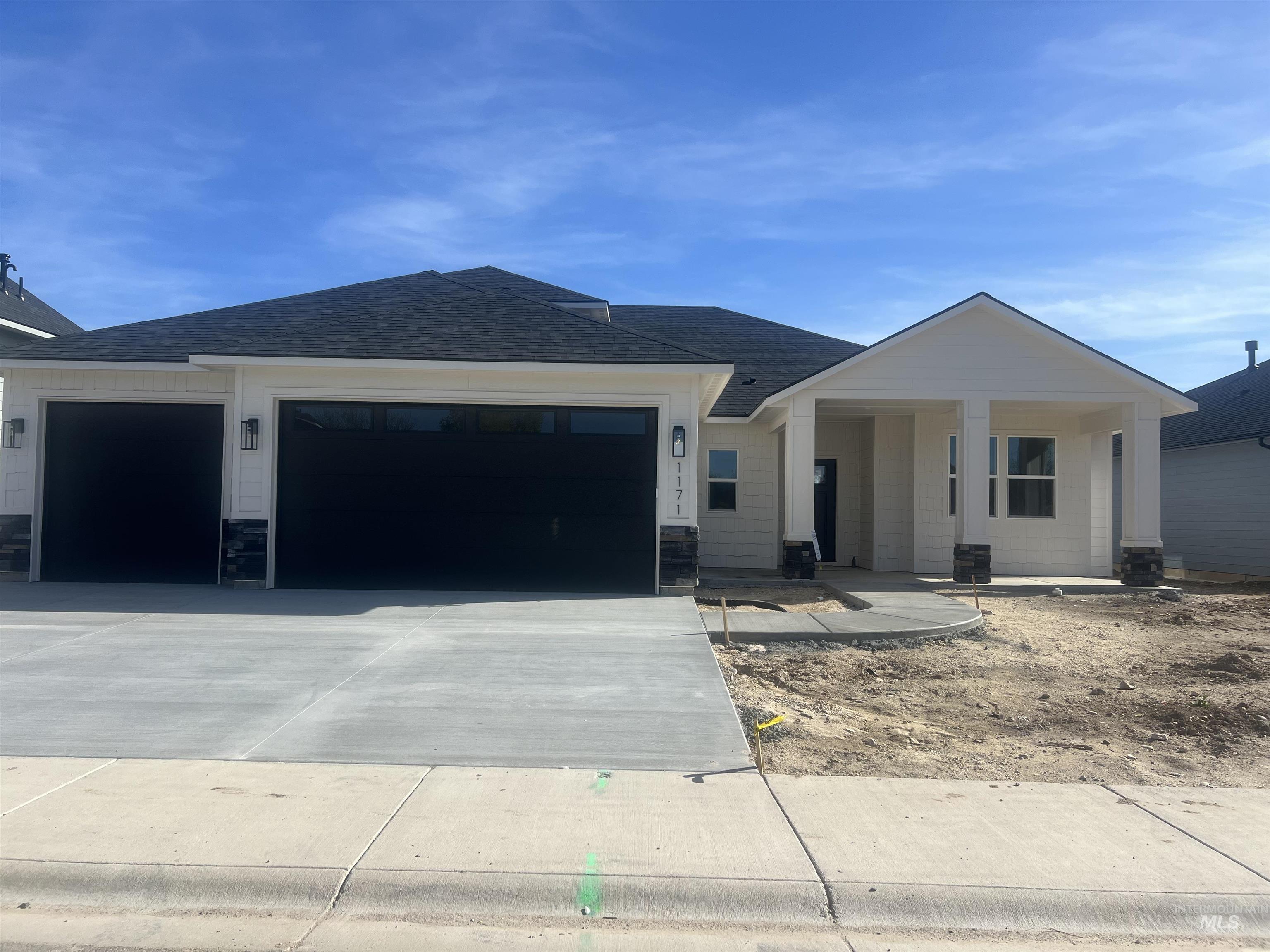 1171 West Recess Way Kuna, ID 83634 - Photo 15 of 15 Modern single-story residence featuring a covered front porch, a two-car garage with black doors, a paved driveway, and stone accents on the porch pillars and garage foundation