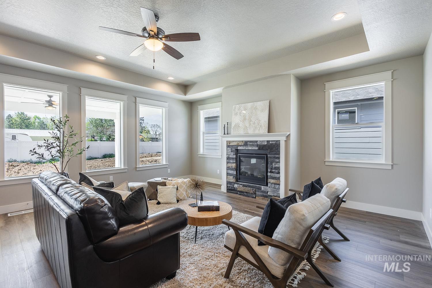 1171 West Recess Way Kuna, ID 83634 - Photo 4 of 28 Living area featuring a stone-clad fireplace with white mantle, recessed lighting, ceiling fan, wood-finish flooring, and multiple windows