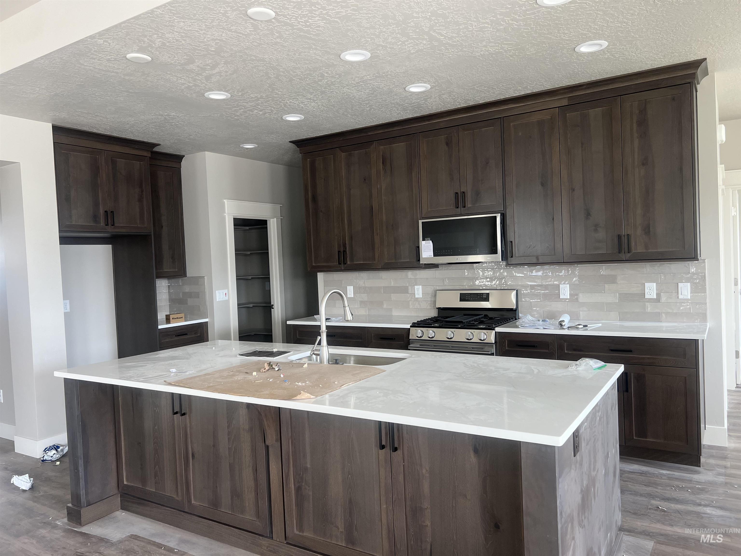 1171 West Recess Way Kuna, ID 83634 - Photo 5 of 15 Kitchen featuring dark wood-type flooring, stainless steel appliances, dark wood finish cabinets, light stone countertops, and a center island with sink