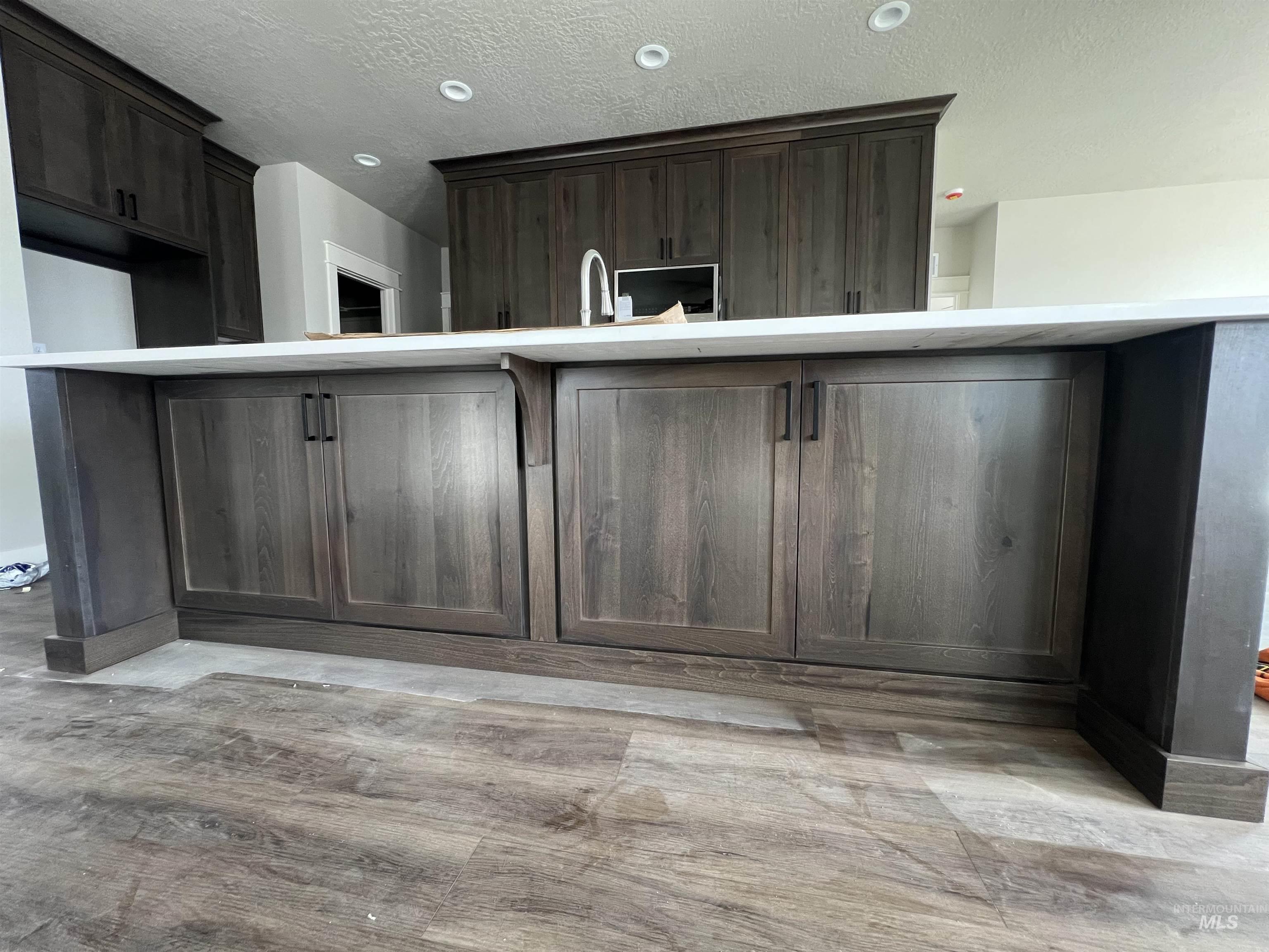 1171 West Recess Way Kuna, ID 83634 - Photo 6 of 15 Kitchen with light wood finished floors, dark wood finish cabinetry, an island with sink, a textured ceiling, and recessed lighting