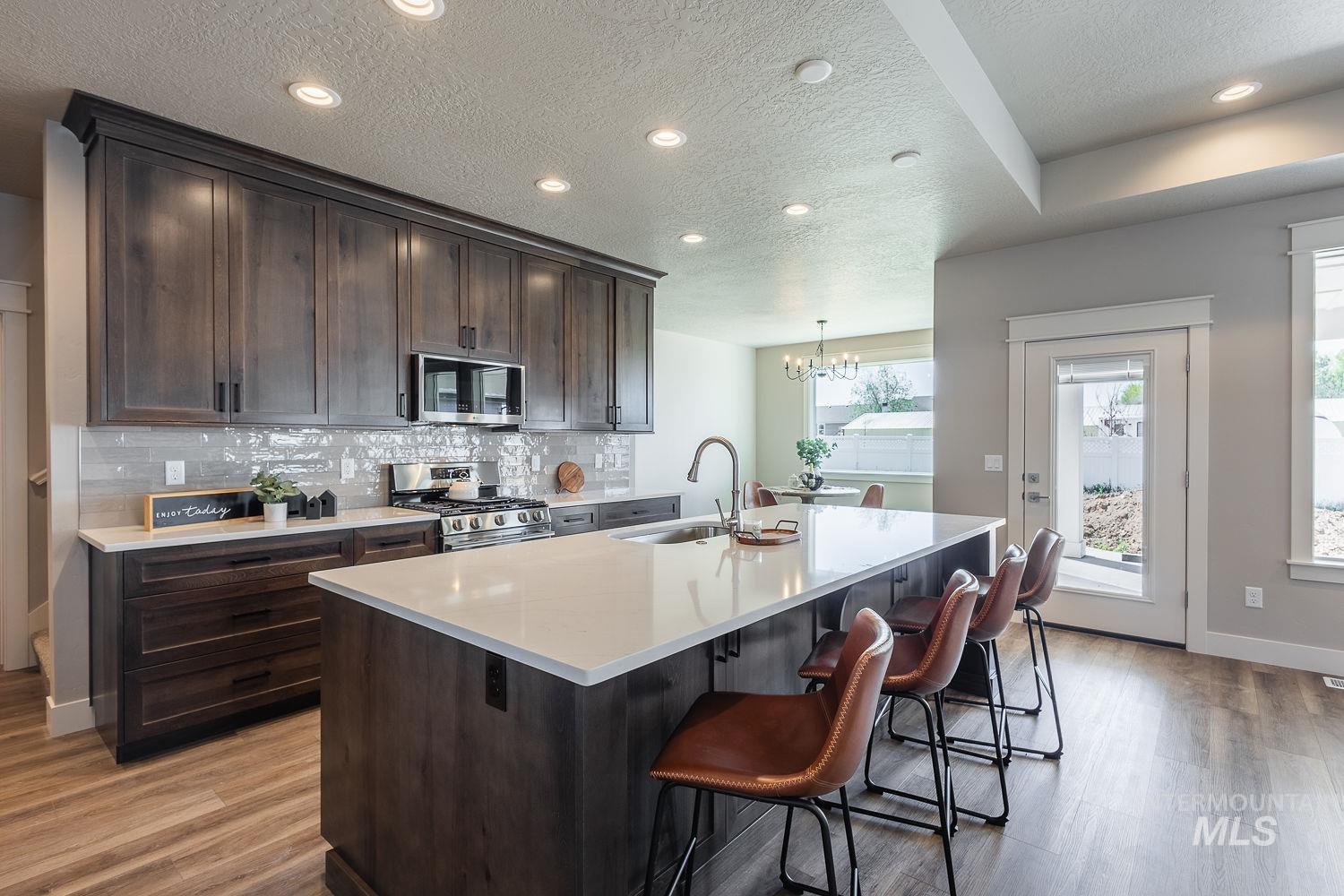 1171 West Recess Way Kuna, ID 83634 - Photo 7 of 28 Spacious kitchen featuring dark wood-finish cabinetry, a large center island with counter seating, stainless steel appliances, a tile backsplash, and light-tone countertops